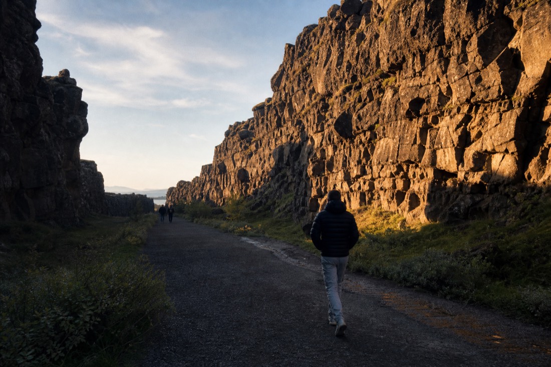 Low midsummer evening light raking across the Almannagjá canyon walls at Þingvellir with an empty path below