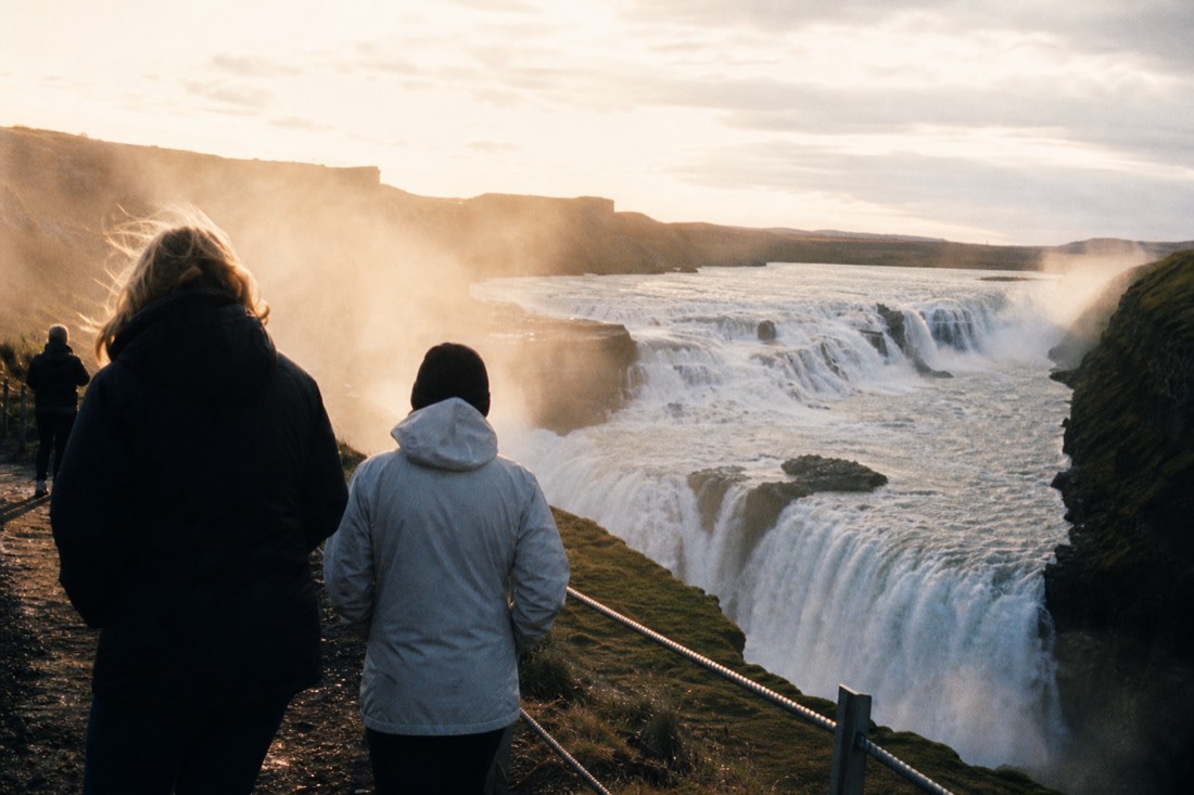 Gullfoss waterfall dropping in two tiers into its canyon with spray drifting over visitors on the upper path