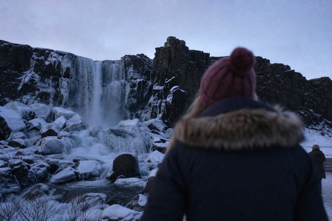 Öxarárfoss waterfall at Þingvellir falling over the dark rift wall onto snow-dusted boulders at winter dusk