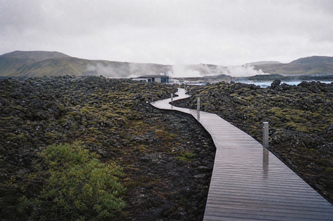 Wooden boardwalk winding through steaming lava rock toward the Blue Lagoon entrance in low evening light