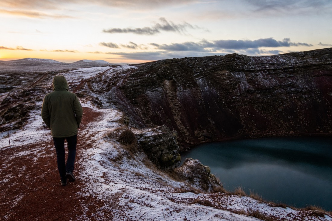 Red volcanic gravel path along the rim of Kerið crater above its aquamarine lake in winter dusk
