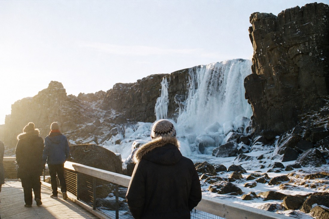 Öxarárfoss waterfall at Þingvellir partly frozen, low golden midday sun raking across the basalt