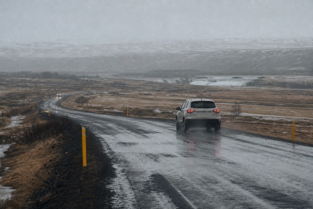 Road 35 near Faxi waterfall lined with yellow snow poles, wet asphalt streaked with slush