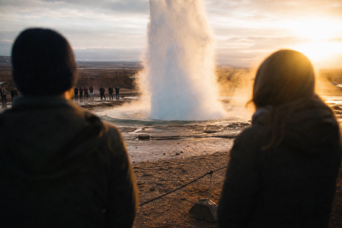Small crowd waiting at a safe distance around the Strokkur geyser vent in low golden evening light