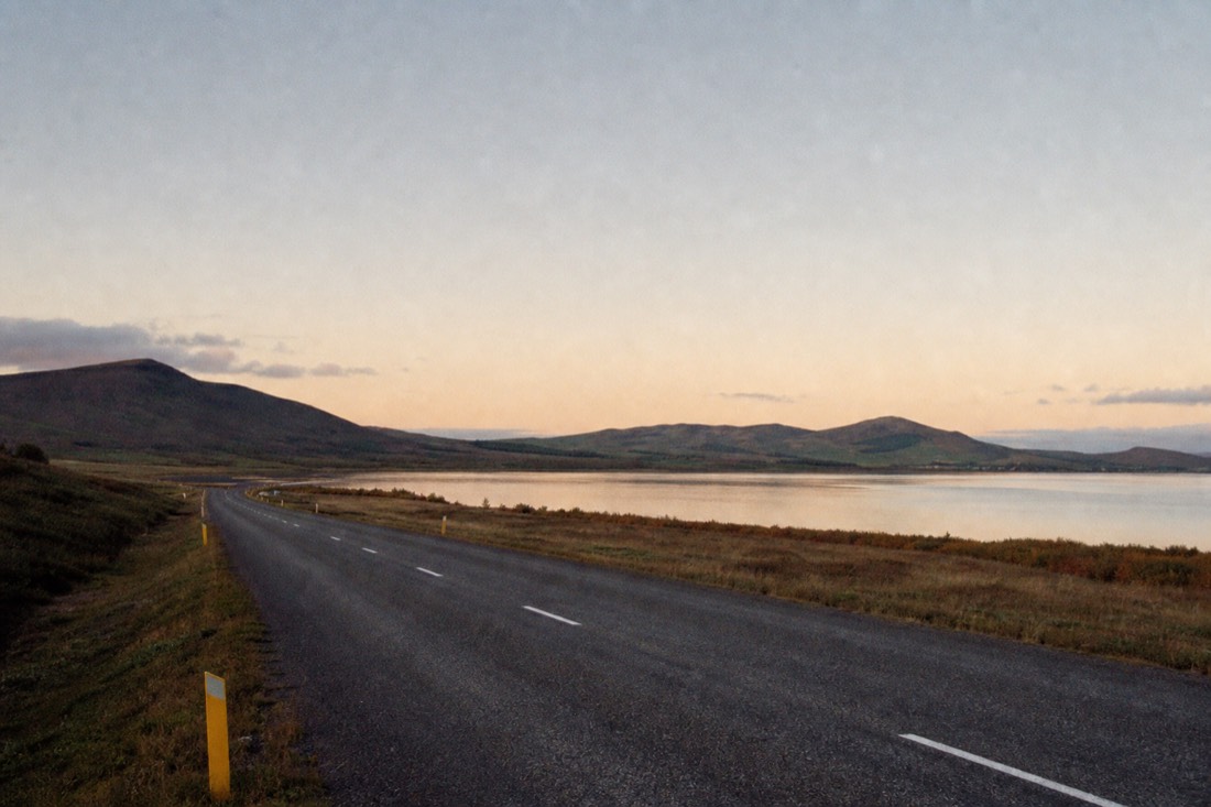 Quiet paved Golden Circle road running past Laugarvatn lake under fading evening light