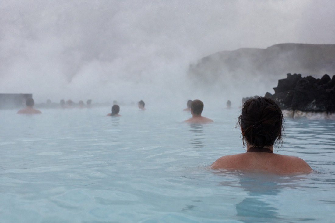 Bathers seen from behind in the milky steaming water of the Blue Lagoon in light drizzle