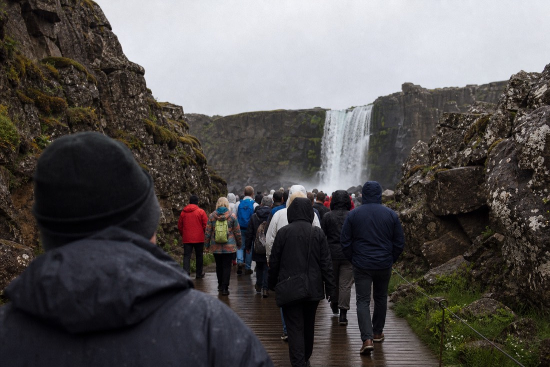 Visitors walking the path toward Öxarárfoss at Þingvellir on an overcast noon