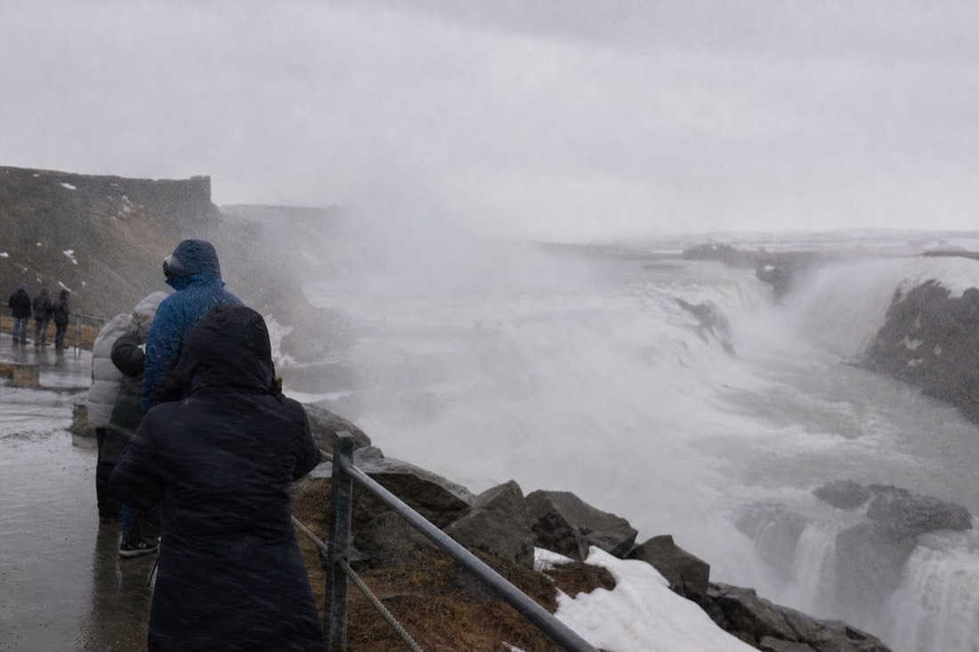 Wind driving spray across the upper viewing platform at Gullfoss under a grey winter sky