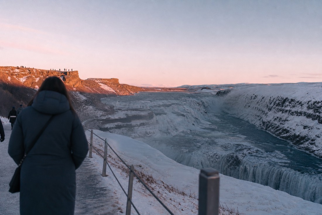 Gullfoss half frozen at winter midday with pink light on the ice ledges of the canyon