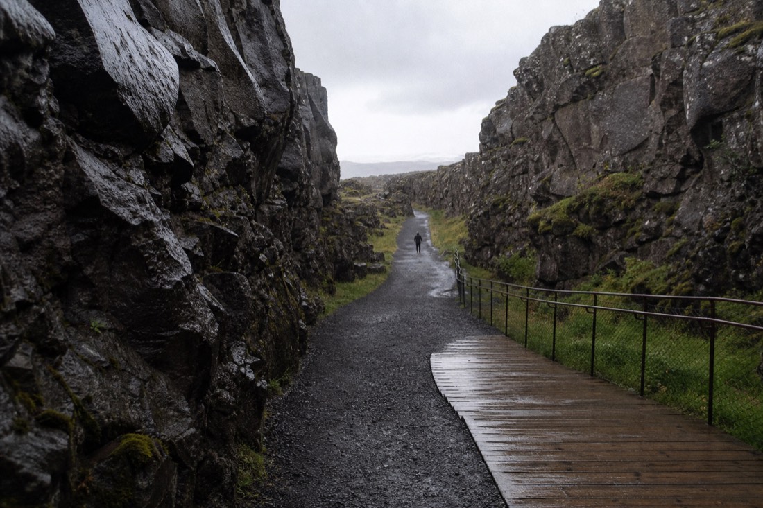 The boardwalk and gravel trail descending through Almannagjá at Þingvellir in light drizzle with wet basalt walls