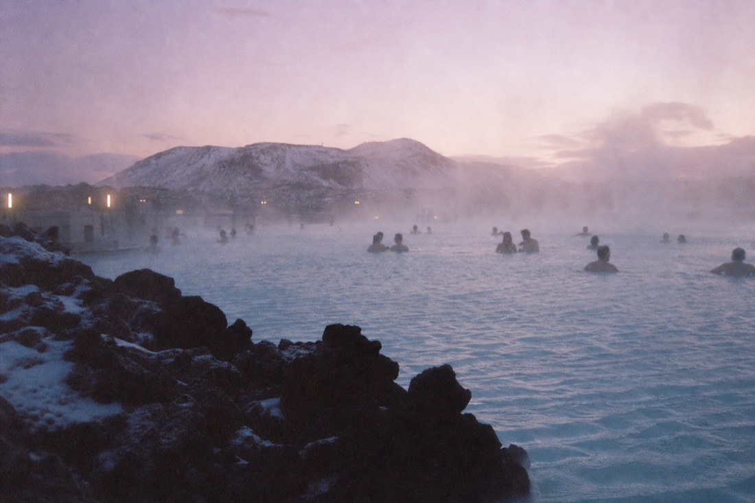 Steam drifting over the milky blue water of the Blue Lagoon at dusk with lava rock in the foreground
